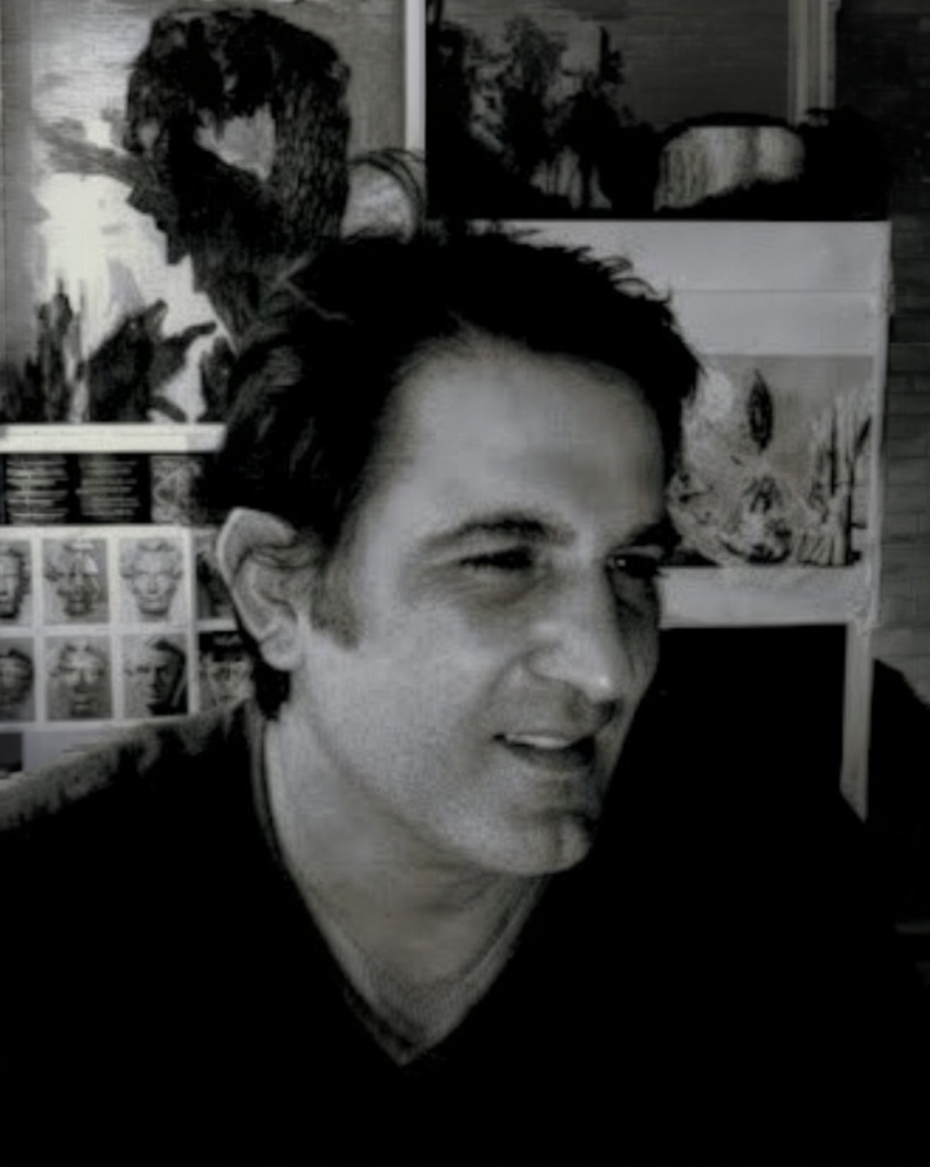 A black and white portrait of a man in profile, with framed artwork and sketches visible in the background.